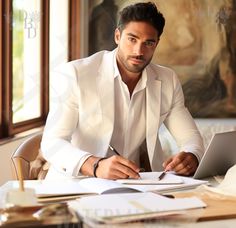 a man sitting at a table with a laptop and papers in front of him, writing on a piece of paper