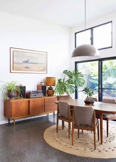 a dining room table with chairs and plants on it in front of a large window