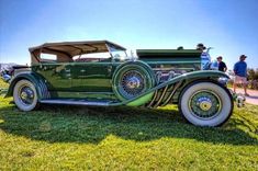 an antique green car parked on top of a lush green field