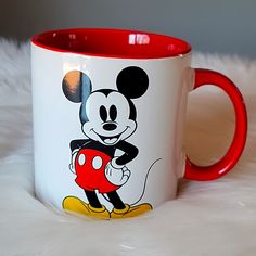 a red and white mickey mouse mug sitting on top of a fur covered bed next to a window