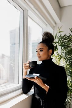 a woman is holding a cup and saucer in her hand while looking out the window