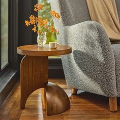 a small table with flowers on it next to a chair in front of a window