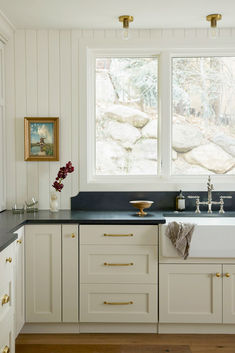 a white kitchen with black counter tops and gold pulls on the cabinet doors is pictured in this image