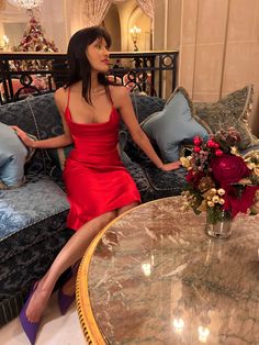 a woman in a red dress sitting on a couch next to a table with flowers