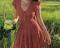 a woman in an orange crochet dress holding a bouquet of flowers standing in a field