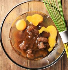 a glass bowl filled with meat and vegetables on top of a wooden table next to two green stalks