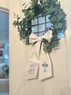 a wreath hanging on the side of a door with a monogrammed bow tied to it