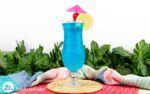 a blue drink sitting on top of a table next to green plants and pillows in front of it