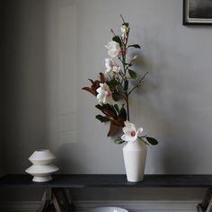 a white vase with flowers sitting on a table next to a bowl and lamp shade