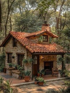 a small stone house in the woods with potted plants on the porch and brick roof