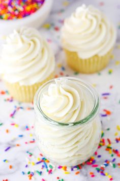 three cupcakes with white frosting and sprinkles on the table