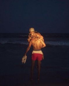 a man standing on top of a beach next to the ocean holding a woman in his arms