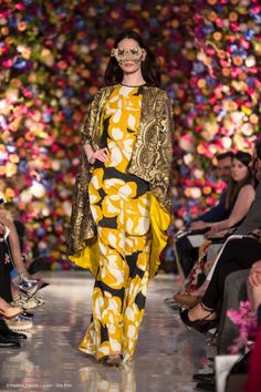 a model walks down the runway in a yellow and black outfit with flowers on it