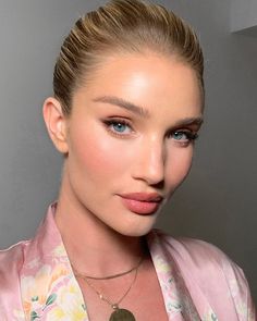 a woman with blonde hair and blue eyes is wearing a pink floral shirt, necklace and earrings