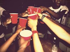 a group of people holding red cups in the middle of their hands, all around one another