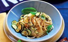 a bowl filled with pasta and zucchini on top of a blue table cloth