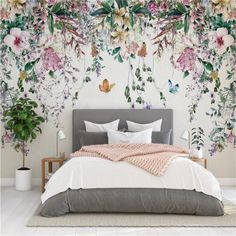 a bed sitting under a wall covered in lots of pink and green flowers next to a plant