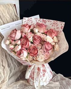 a bouquet of pink and white roses sitting on top of a table next to an envelope