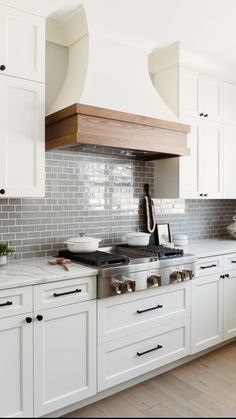 a kitchen with white cabinets and stainless steel range hoods over the stove, along with wooden flooring