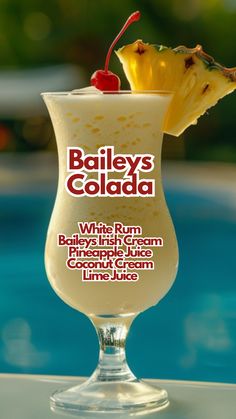 a close up of a drink on a table next to a swimming pool with the words baileys colada written in it