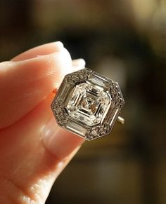 a close up of a person's hand holding an engagement ring with a diamond in it