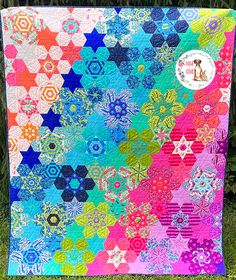 a multicolored quilt with stars and circles on the front, sitting in grass