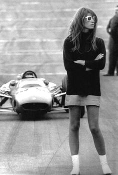 a woman standing next to a race car on a track with her arms crossed in front of her