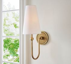 a wall lamp with a white shade on it next to a window in a room