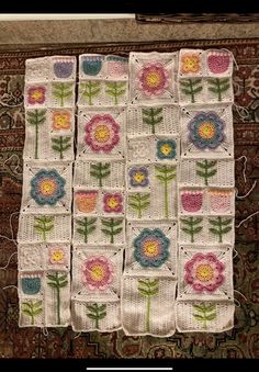 four crocheted squares with flowers on them sitting on top of a rug in front of a fireplace