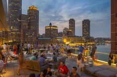 many people are sitting at tables on the roof of a building with city lights in the background