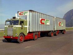 a green and red semi truck driving down the road with mountains in the back ground