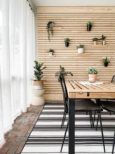 a wooden table with black chairs and potted plants on the wall in front of it