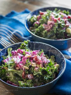 two blue bowls filled with salad on top of a wooden table next to a fork