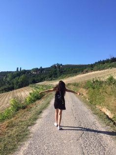 a woman walking down a dirt road with her arms outstretched