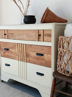 a white dresser with wooden drawers next to a wicker basket and vase on top