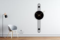 a black clock on the wall next to a chair and floor lamp in a room