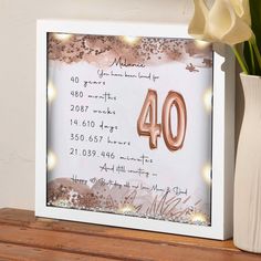 a white vase filled with flowers next to a framed birthday card that reads 40 years