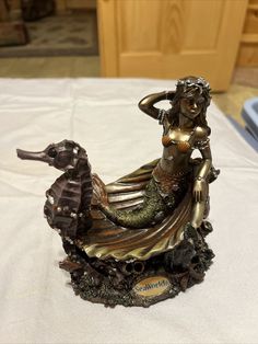 a statue of a mermaid riding a sea horse on a white sheet covered tablecloth