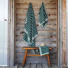 two green and white towels hanging on the wall next to a wooden bench in front of a door