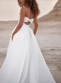 a woman in a white wedding dress standing on the beach with her back to the camera