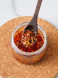 a spoon in a jar filled with food on top of a cork place mat next to a bottle opener