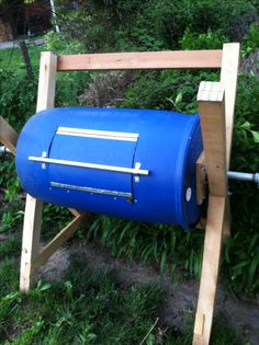 a blue barrel sitting on top of a wooden stand in the middle of some grass