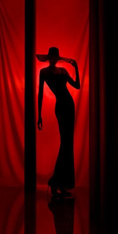 the silhouette of a woman wearing a hat in front of a red curtain with curtains behind her