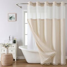 a bath tub sitting next to a window covered in a white shower curtain with tassels