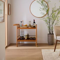 a bar cart with bottles and glasses on it in front of a mirror, potted plant and chair