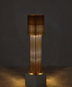 a tall wooden lamp sitting on top of a white pedestal next to a black wall