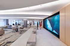 people are standing in an office lobby with large screens on the wall and couches