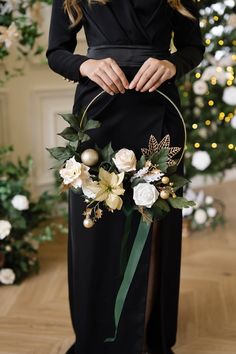 a woman wearing a black dress holding a flower arrangement in front of a christmas tree