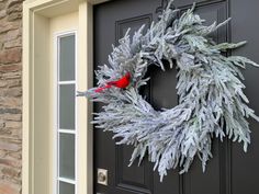 a christmas wreath with a cardinal sitting on it's front door, in front of a house