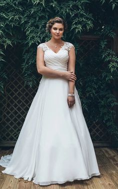 a woman standing in front of a bush wearing a white dress and holding her hand on her hip